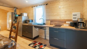 Eine kleine Küche mit Holzwänden, einem Kühlschrank, einer Mikrowelle, einer Kaffeemaschine und einem Spülbecken.