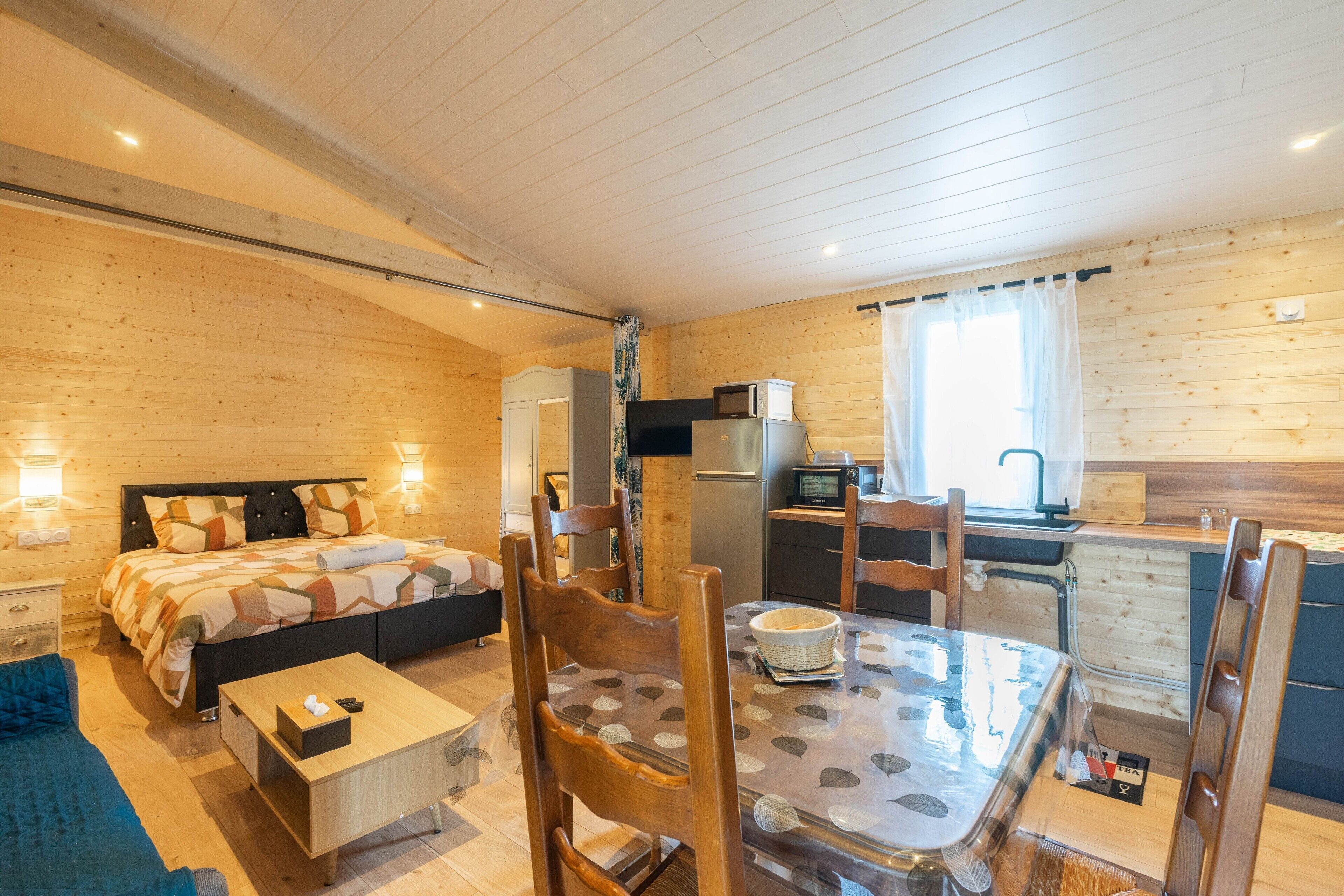 Una cabaña de madera con una cama, una mesa de comedor, sillas, una cocina y una pequeña sala de estar.