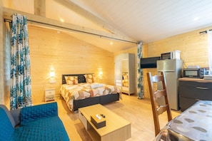 A cozy room with a bed, a sofa, a table, a chair, a kitchenette, and a wardrobe.
