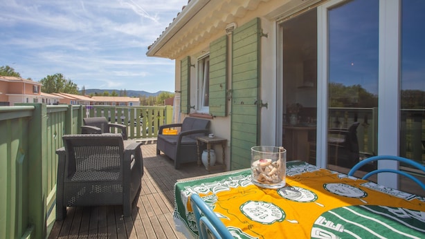 A deck with outdoor furniture, a table with a patterned tablecloth, and a view of the surrounding area.
