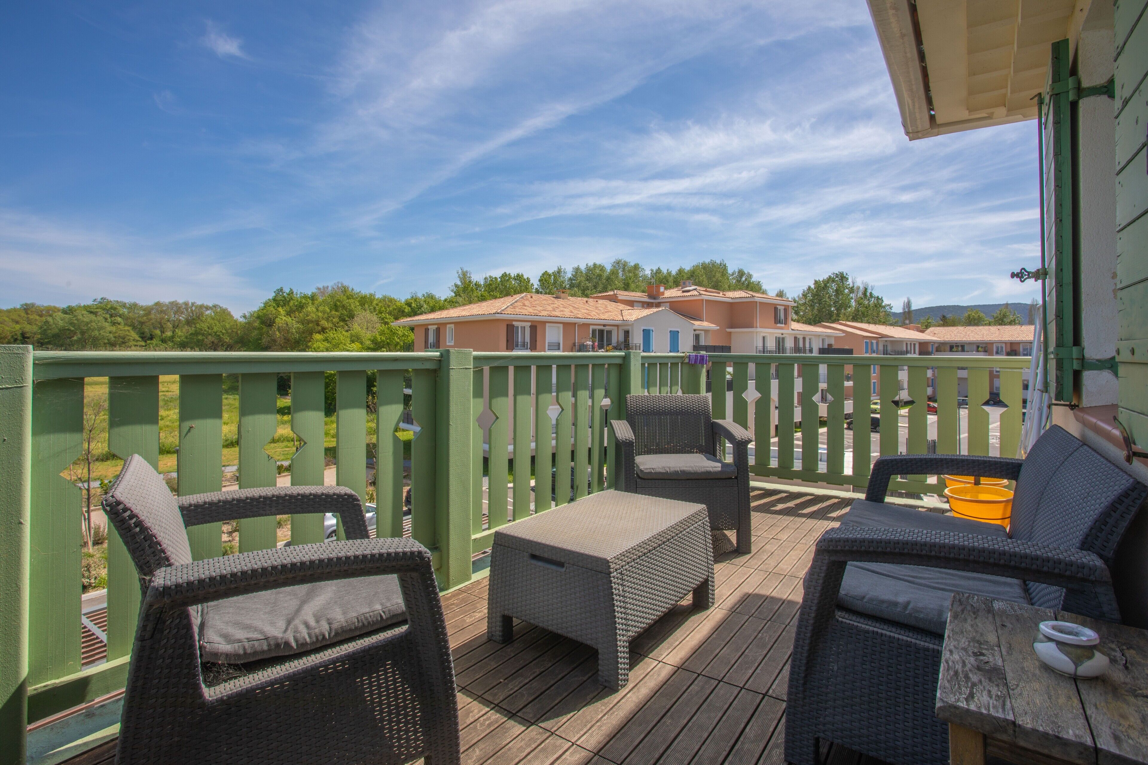A deck with wicker furniture, a table, and a view of buildings in the background.