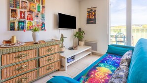 A modern living room with a television, wicker furniture, a colorful rug, and a balcony view.