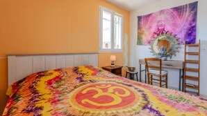 A bedroom with a bed, a desk, a chair, a window, and a tapestry.