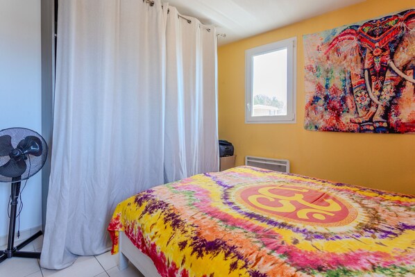A room with a bed, a fan, a window, and a wall painting. - Apartment 'Au Calme Avec Terrasse' with Private Terrace and Wi-Fi (Cogolin)