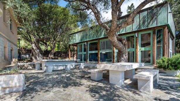 A courtyard with stone benches and a building with large windows. - Apartment 'La Vela Rossa' with Shared Pool, Wi-Fi and Air Conditioning (Sas Linnas Siccas)