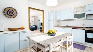 A modern kitchen with light blue cabinets, a granite countertop, and a dining table with chairs. - Apartment 'La Vela Rossa' with Shared Pool, Wi-Fi and Air Conditioning (Sas Linnas Siccas)
