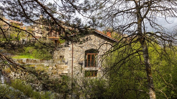 Un edificio de piedra con un pequeño balcón, rodeado de árboles y follaje.