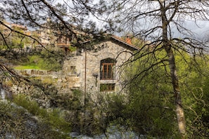 Un edificio de piedra con un pequeño balcón, rodeado de árboles y follaje.