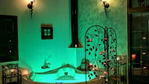 Habitación con un jacuzzi, dos lámparas fijadas a la pared, un ventanal pequeño y una planta decorativa.