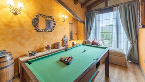 Una mesa de billar en una habitación con vigas de madera, un espejo grande y vistas al exterior por una ventana.