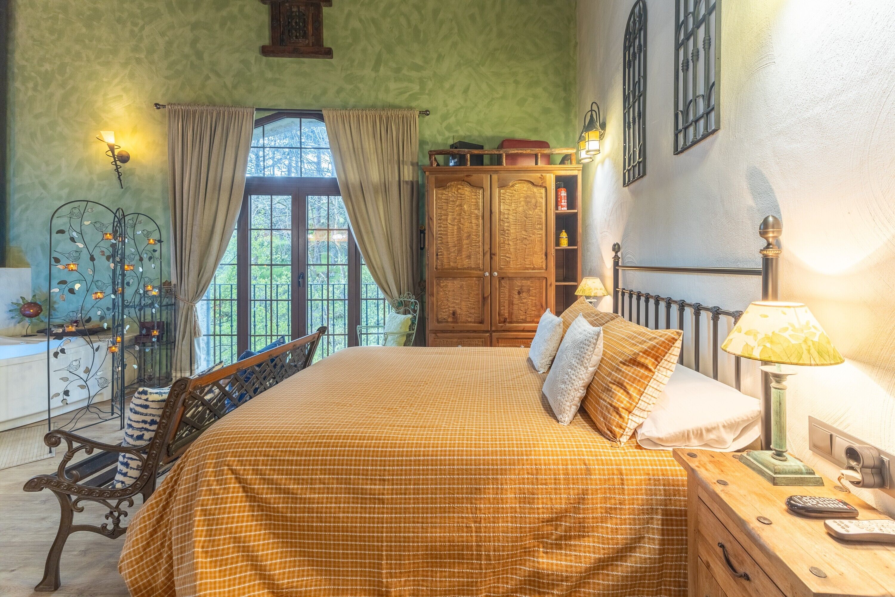 A bedroom with a bed, bedside table, lamp, and a view of the outdoors.