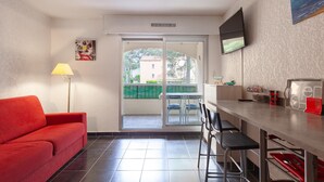 A room with a red sofa, a dining table with chairs, a TV mounted on the wall, and a sliding glass door leading to an outdoor area.