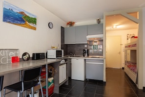 A compact kitchen with a microwave, toaster, and sink. There's a small refrigerator, a dining area with a chair, and a bunk bed in the adjacent room. - Studio 'Chez Alain Et Martine' with Private Terrace (Saint-Mandrier-sur-Mer)