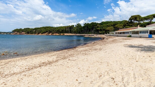 A beach with clear water, a sandy shore, and a building with a green roof.