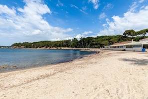 A beach with clear water, a sandy shore, and a building with a green roof. - Studio 'Chez Alain Et Martine' with Private Terrace (Saint-Mandrier-sur-Mer)