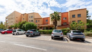 A parking lot with several cars, a building with a red roof, and a palm tree.