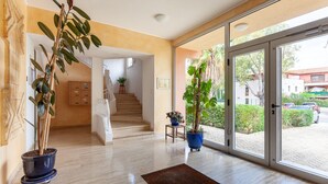 A spacious indoor area with a staircase, potted plants, and a view through large glass doors.