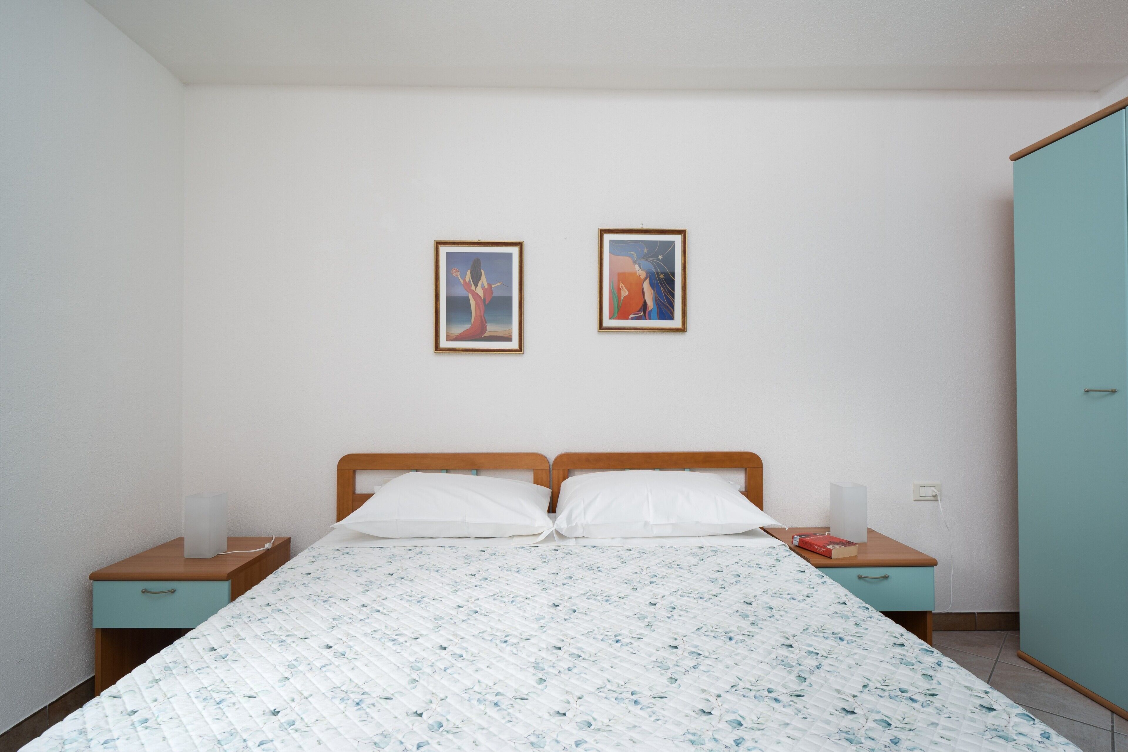 Ein Schlafzimmer mit einem Bett, zwei Nachttischen, einem Kleiderschrank und zwei gerahmten Bildern an der Wand.