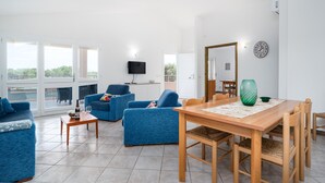 Una sala de estar moderna con una mesa de comedor de madera, sofás azules, un televisor de pantalla plana y ventanas amplias.