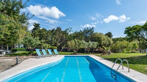 Una piscina con mosaicos azules, dos sillas de descanso y una escalera metálica.