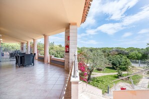 A covered outdoor area with a fire extinguisher, a table with chairs, and a view of a landscaped garden.