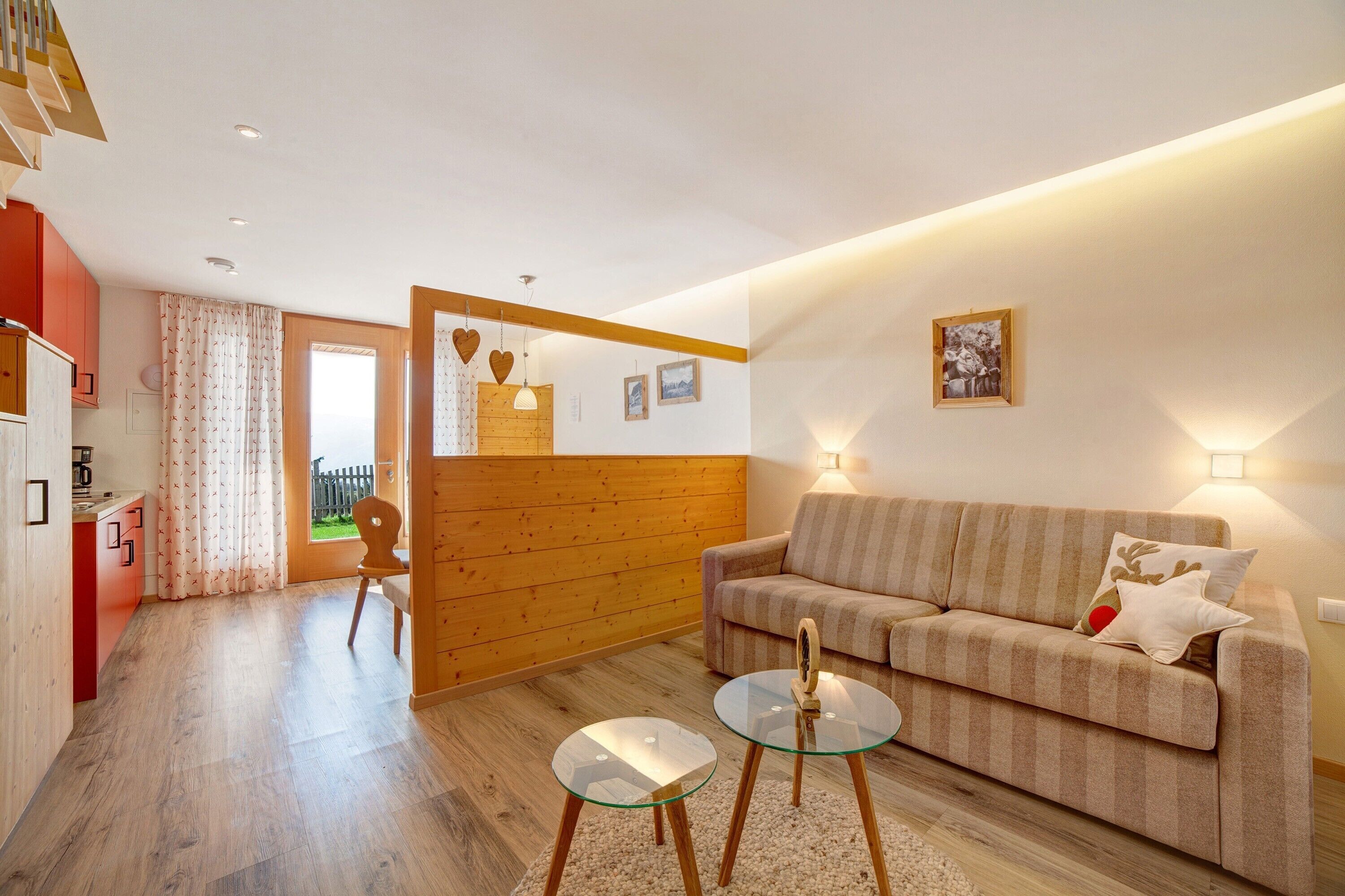 Un salon moderne avec un canapé, une table basse en verre, des éléments décoratifs en bois et une vue sur l’extérieur, visible à travers une porte.