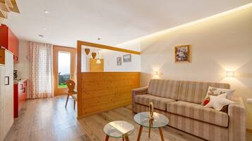 Un salon moderne avec un canapé, une table basse en verre, des éléments décoratifs en bois et une vue sur l’extérieur, visible à travers une porte.