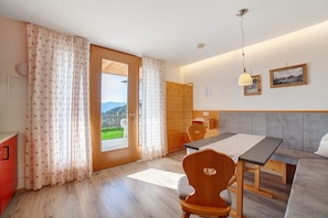 A room with a wooden dining table, a wooden chair, a sofa, a wooden cabinet, and a view of the outdoors.