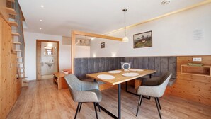 A modern kitchen with a dining table, two chairs, a bench, and a wooden staircase.