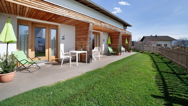 A modern house with a covered patio, outdoor seating, and a well-maintained lawn.