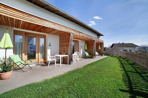 A modern house with a covered patio, outdoor seating, and a well-maintained lawn. - Apartment 'Leben' with Mountain View, Shared Terrace and Wi-Fi (Verano)