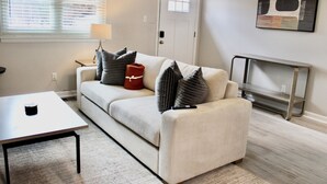 A living room with a beige sofa, striped pillows, a red throw, a white table, and a fireplace. - Charming 2-bedroom townhome in Raleigh with AC, WiFi (Raleigh)