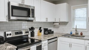 A modern kitchen with white cabinets, stainless steel appliances, and a granite countertop. - Charming 2-bedroom townhome in Raleigh with AC, WiFi (Raleigh)