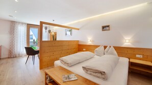 A hotel room with a wooden headboard, a bed with white linens, a wooden bench, a small table with a magazine, and a view of the outside through a window. - Apartment 'Heimat' with Mountain View, Shared Terrace and Wi-Fi (Verano)