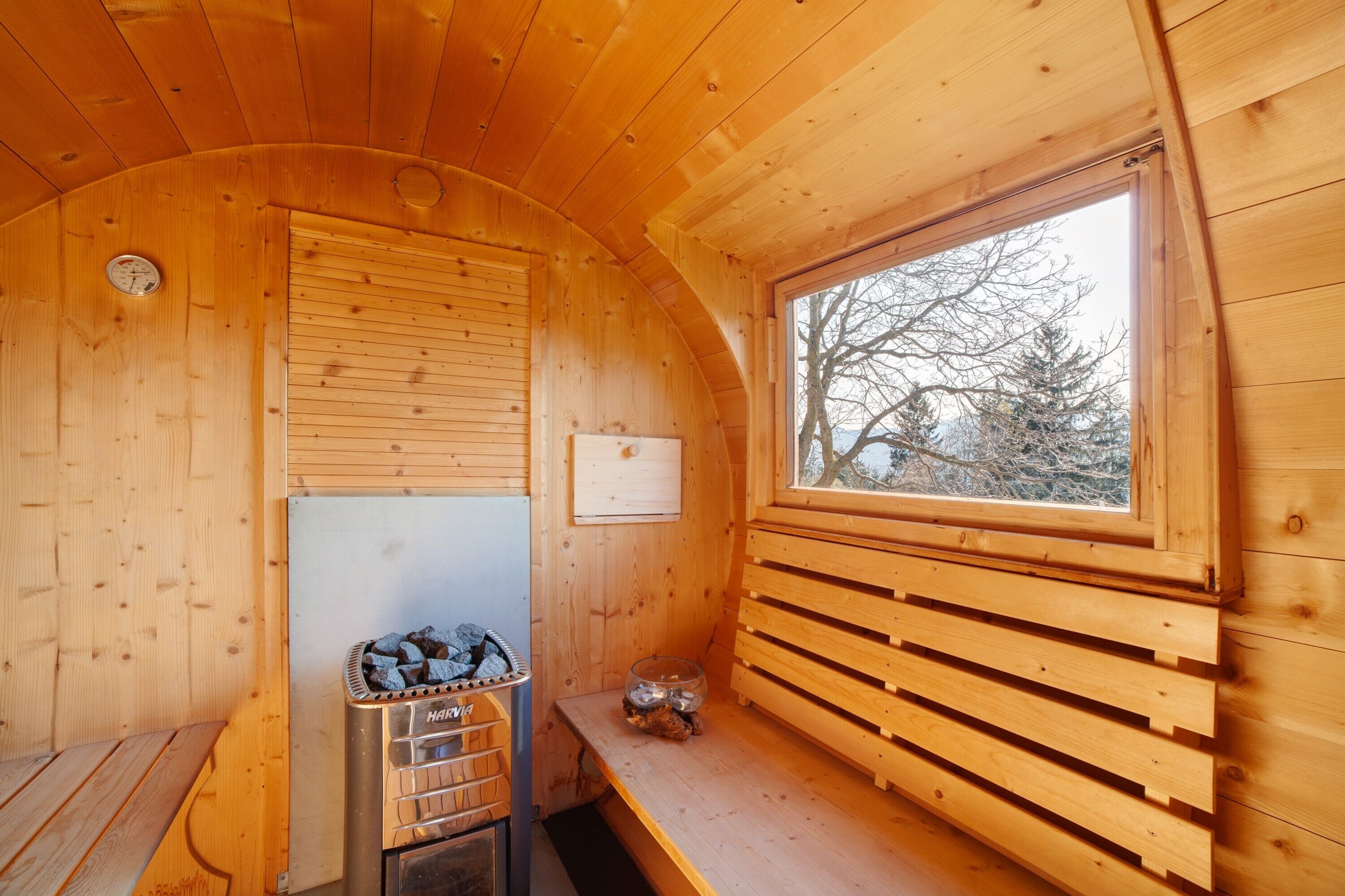 A wooden cabin interior with a sauna, a window with a view of trees, and a wooden bench.