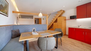 A modern kitchen with red cabinets, a wooden dining table with two chairs, and a staircase leading to an upper level. - Apartment 'Heimat' with Mountain View, Shared Terrace and Wi-Fi (Verano)