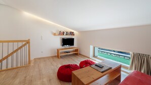 A modern living room with a TV, bookshelves, red bean bags, a wooden coffee table, and a view of a green field. - Apartment 'Heimat' with Mountain View, Shared Terrace and Wi-Fi (Verano)