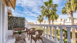 A balcony with wicker furniture, a potted plant, and a view of palm trees and buildings. - Apartment 'A Un Paso Del Mar' with Shared Pool and Balcony (Guardamar del segura)