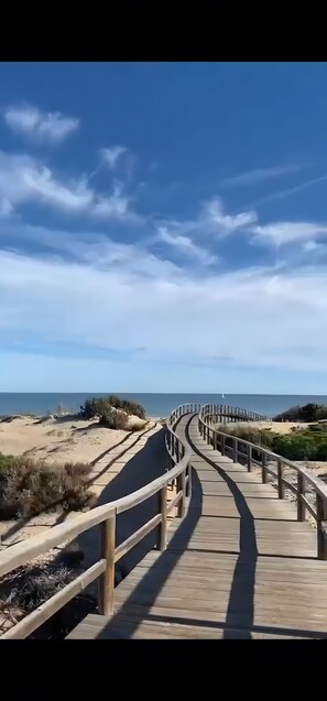 En träpromenad som leder till en strand med sanddyner och gles vegetation.