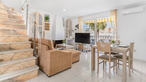 A living room with a marble staircase, a sofa, a TV, a dining table with chairs, and a balcony with yellow curtains. - Apartment 'A Un Paso Del Mar' with Shared Pool and Balcony (Guardamar del segura)