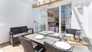 Eine Terrasse mit Esstisch, Korbmöbeln und einer Glastür zu einem Innenraum.
