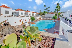 Un área de piscina con una piscina azul cristalina, edificios blancos de techos rojos y una variedad de plantas.