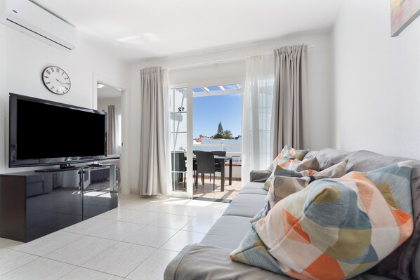 A modern living room with a flat-screen TV, a sofa, and a dining area with a view.