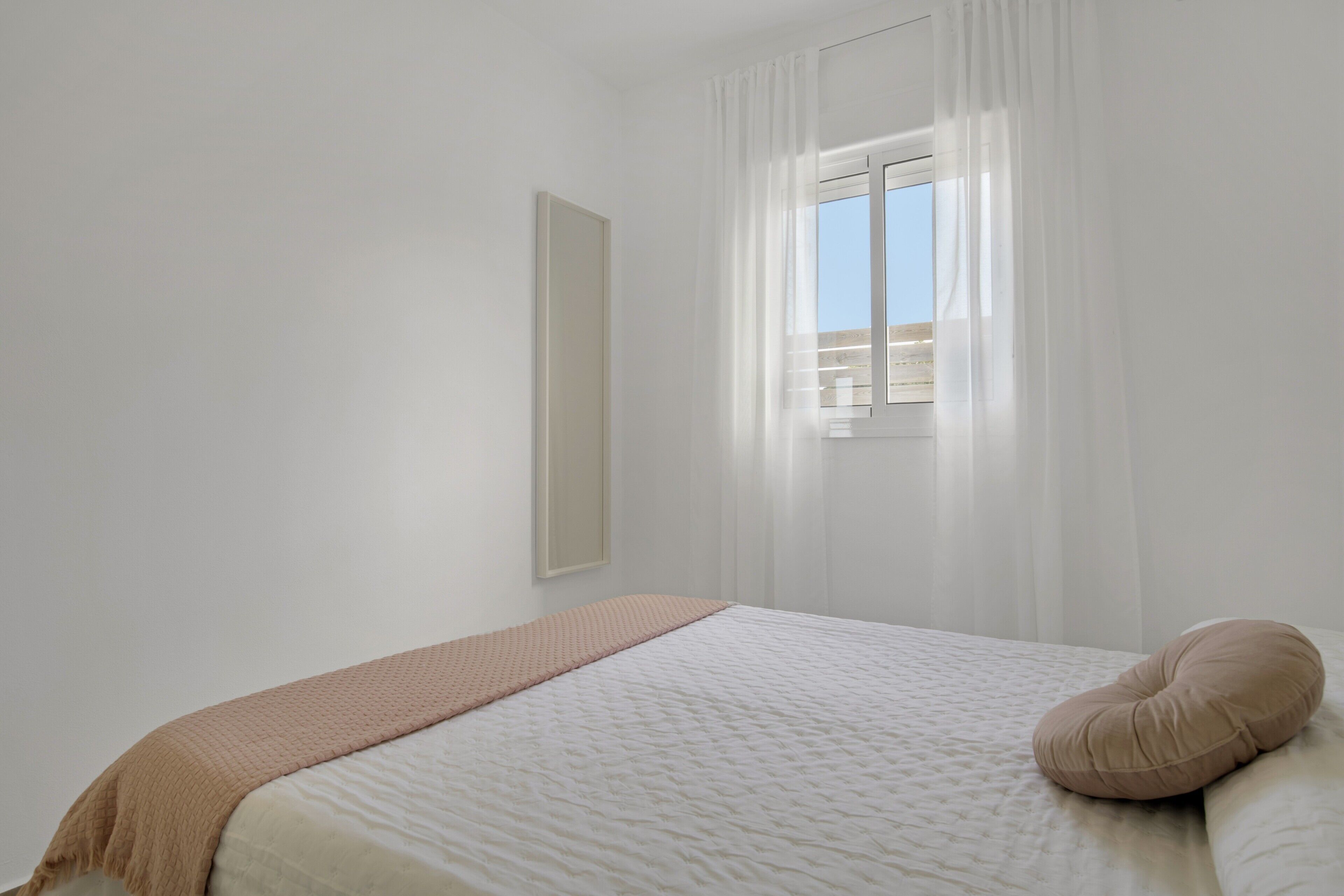 Une chambre à coucher avec un lit, une fenêtre avec des rideaux et un miroir fixé au mur.