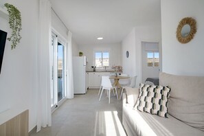 Un interior moderno con sofá, mesa de comedor y sillas, zona de cocina y vistas a través de un ventanal.