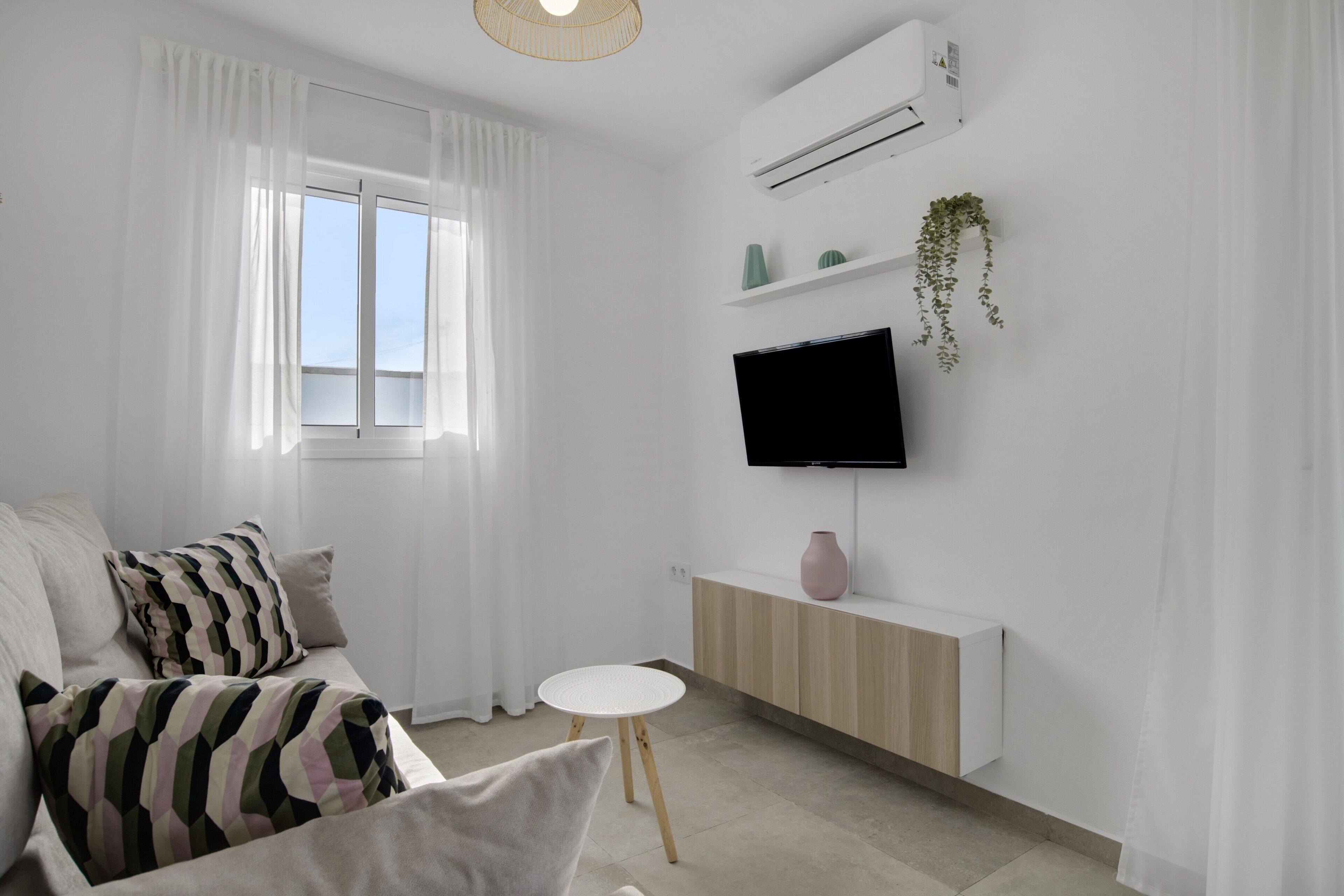 Una sala de estar moderna con un sofá, una mesita redonda, un televisor montado en la pared y un equipo de aire acondicionado.