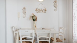 A white dining table with four chairs, a hanging light fixture, and wall decorations including a seahorse and a 'BEACH' sign. - Apartment 'Lumia Sole' with Sea View, Wi-Fi and Air Conditioning (Sciacca)