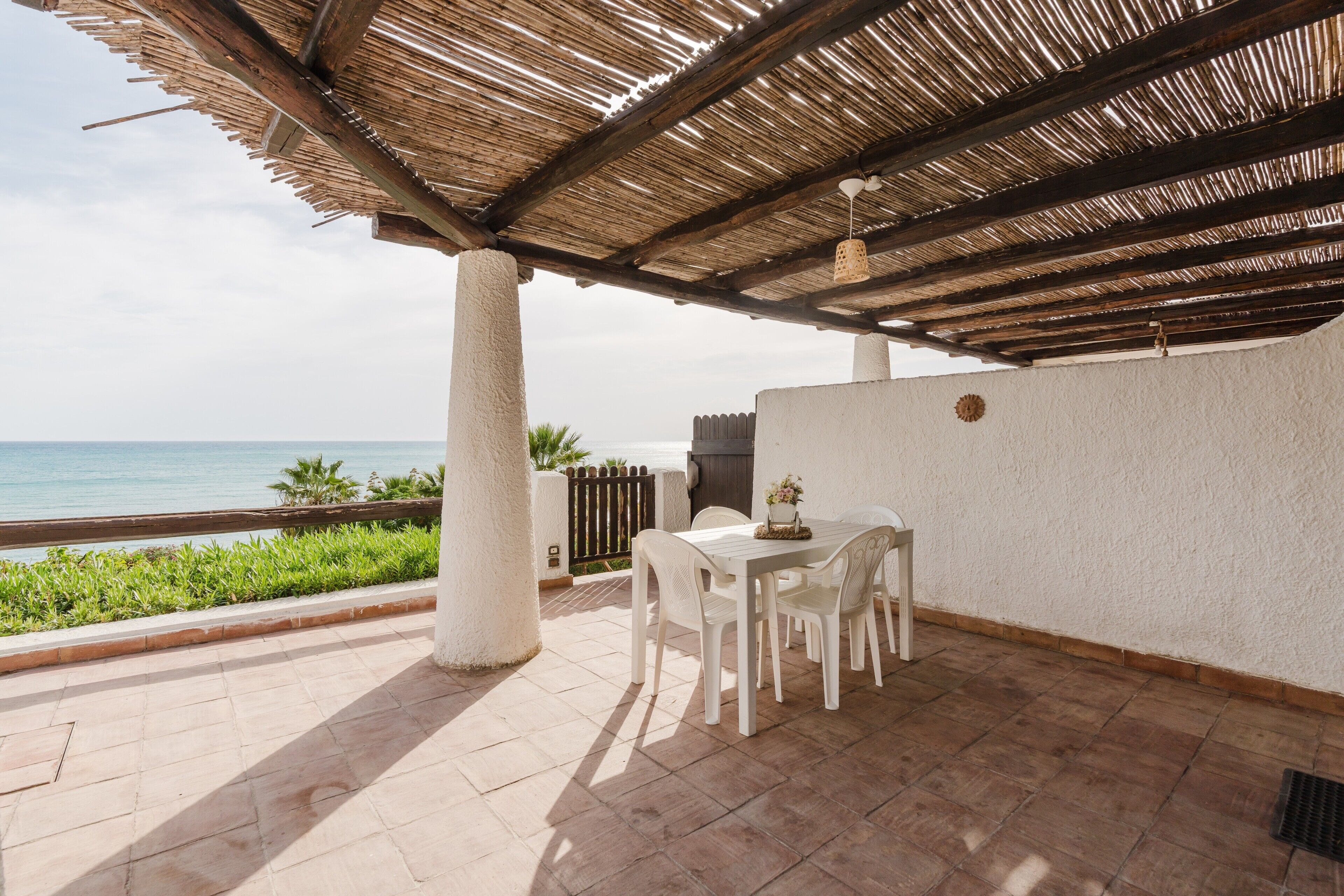 Un patio coperto con tavolo e sedie, vista sul mare e una parete bianca.