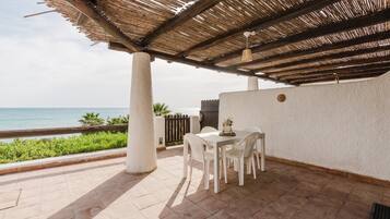 Un patio coperto con tavolo e sedie, vista sul mare e una parete bianca.