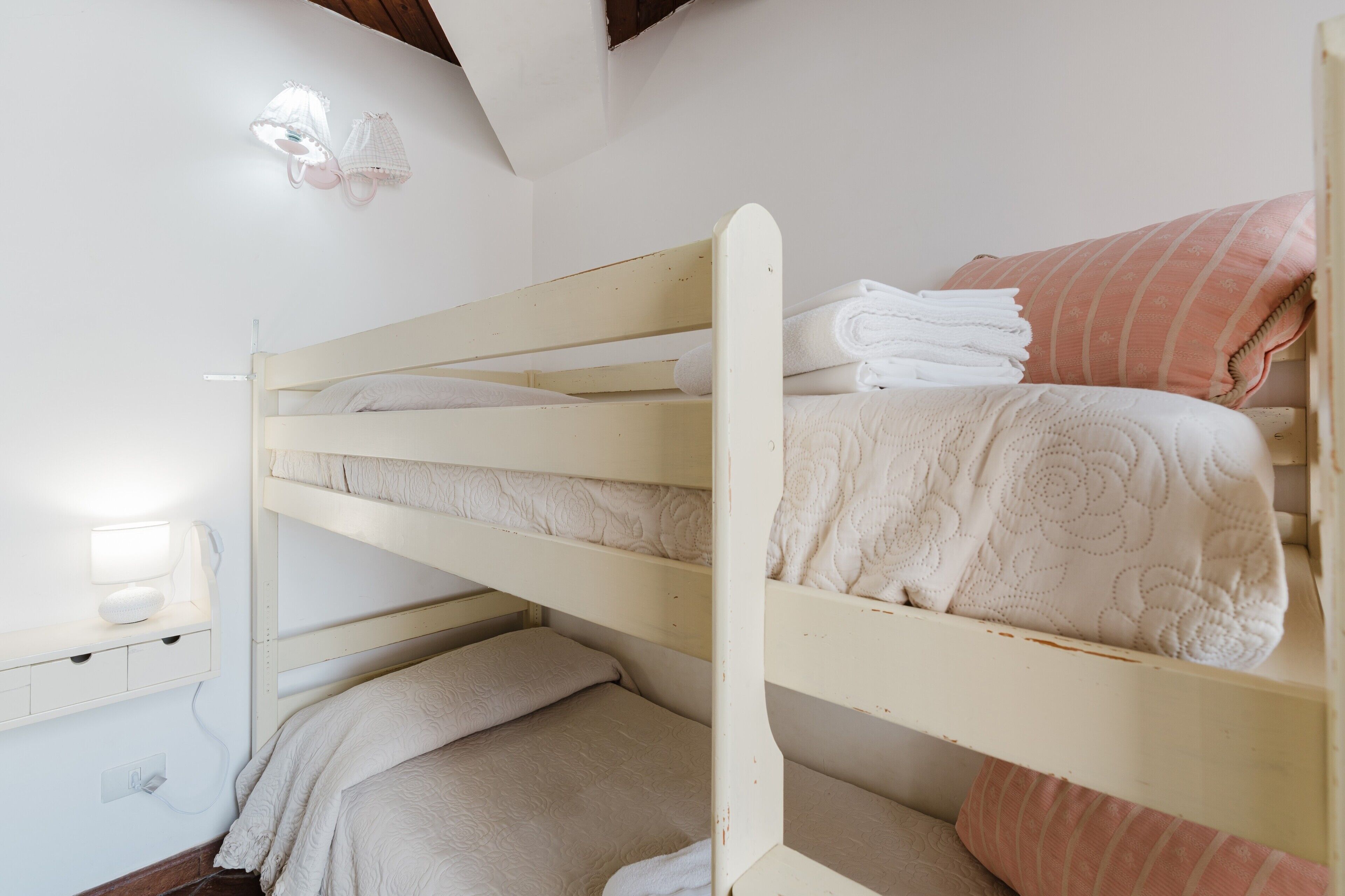 A bunk bed with white bedding, a bedside lamp, and a wall-mounted light fixture.